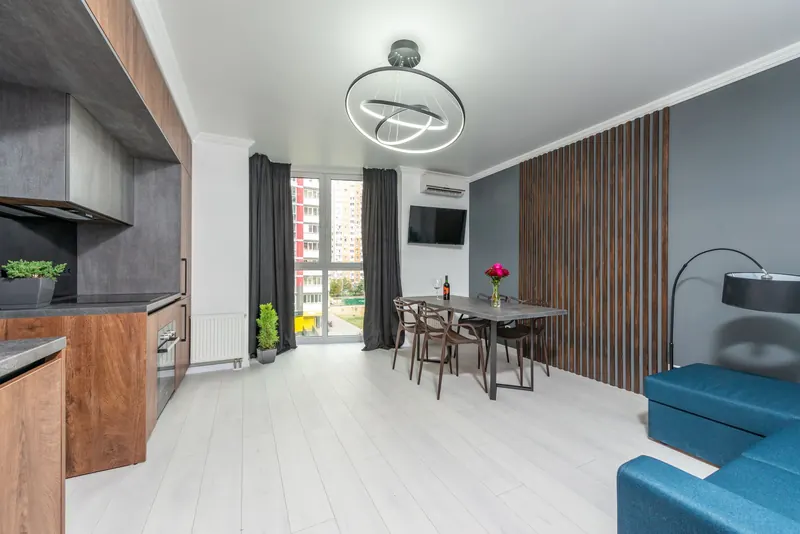 Creative design of kitchen and living room with sofa against table and cabinets on parquet under geometric lamp in flat