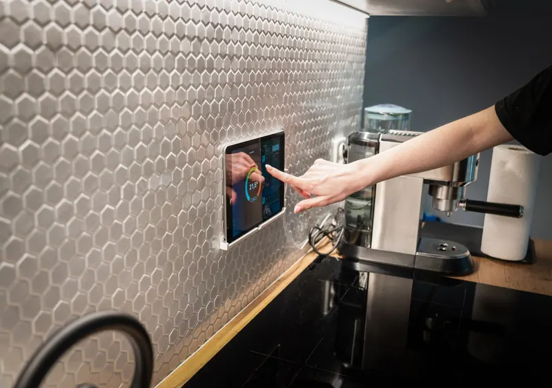 A modern kitchen with a touchscreen smart home control panel integrated into a hexagon-patterned wall