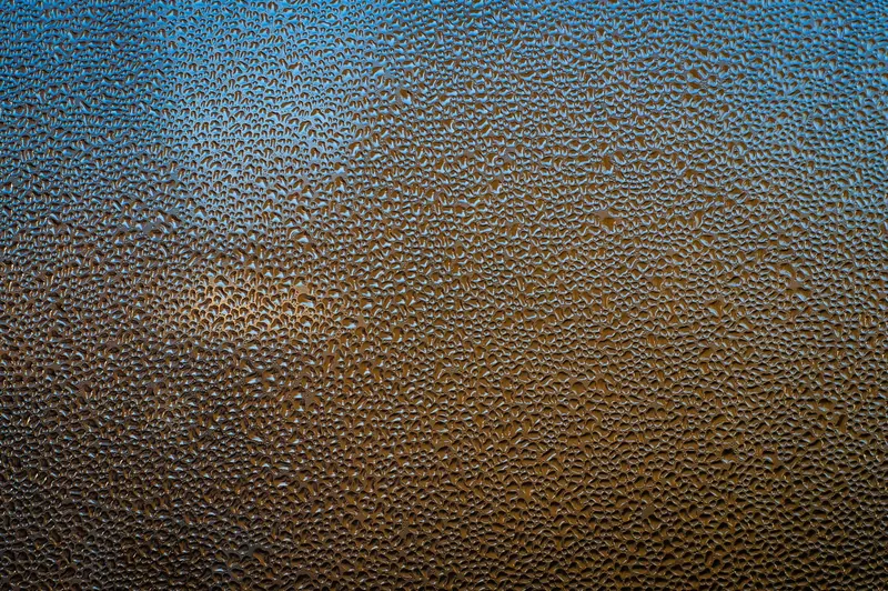 Artistic close-up of condensation forming tiny water droplets on a glass surface with vibrant colors