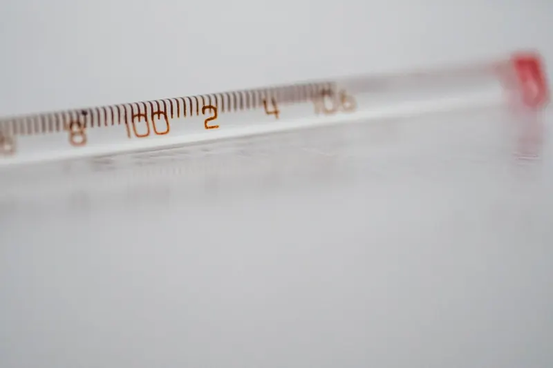 Detailed close-up of a mercury glass thermometer on a white surface, showing temperature measurements