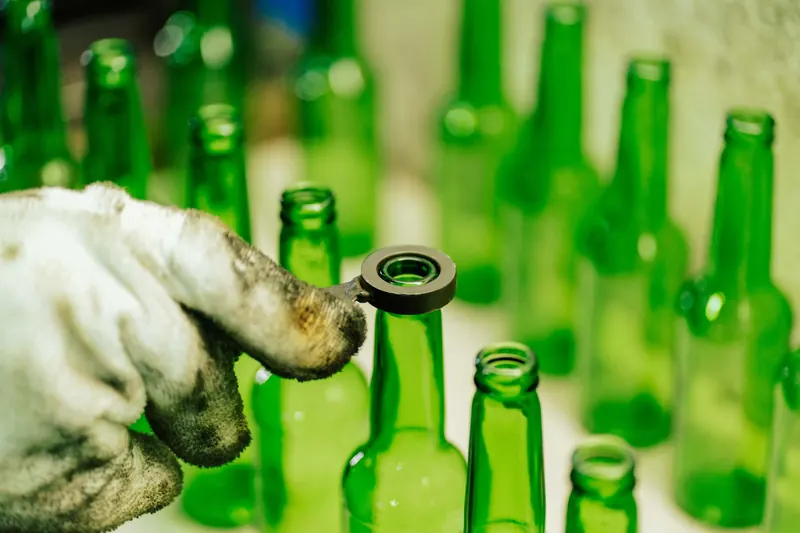 Close-up of a worker handling green glass bottles in a factory setting in Tanzania
