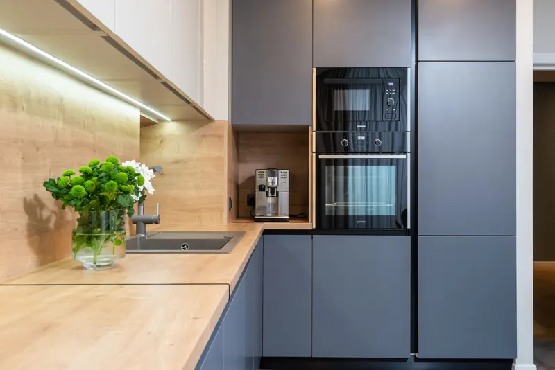 Creative design of kitchen with built in oven against coffee machine and flowers in vase on table in house